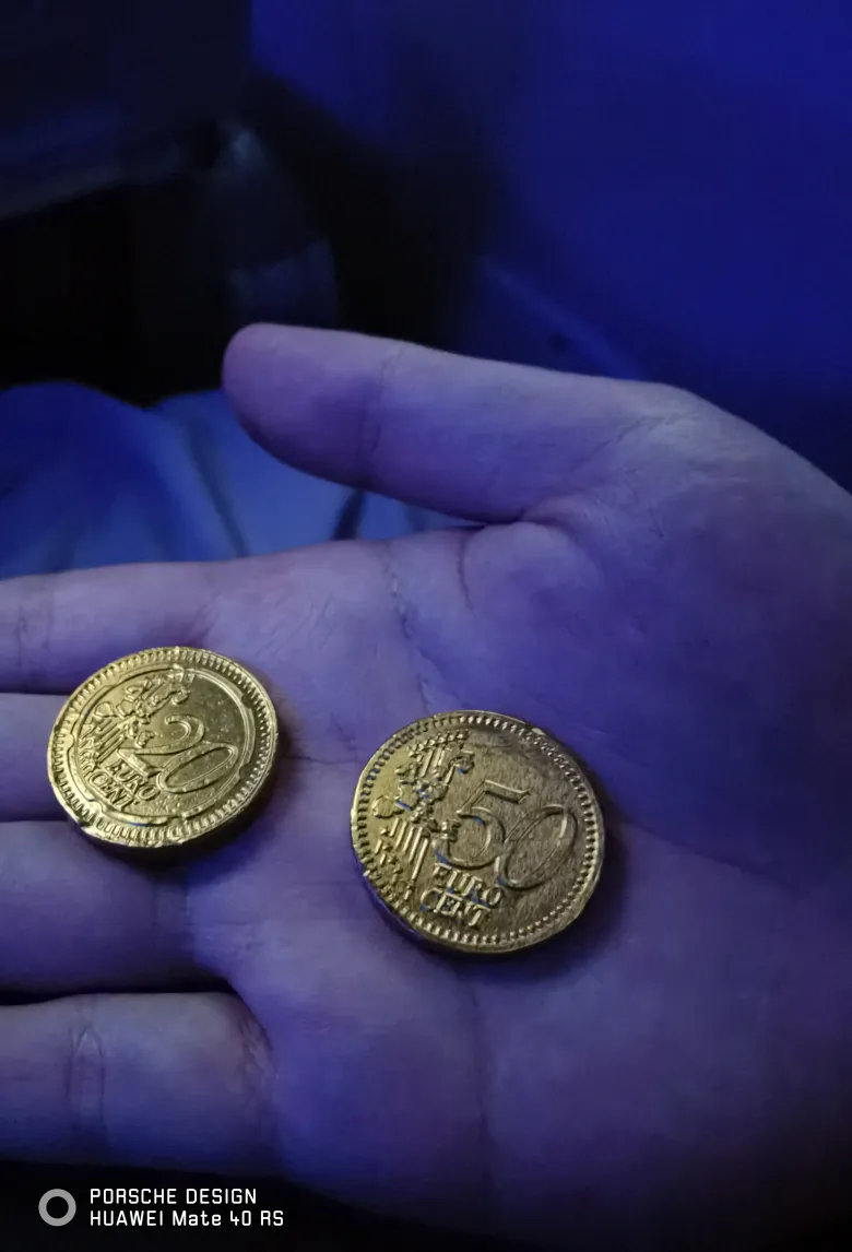 照片：蓝色灯光下摊开的手掌里放着两枚金箔巧克力币，分别印着 20 与 50 EURO CENT。
