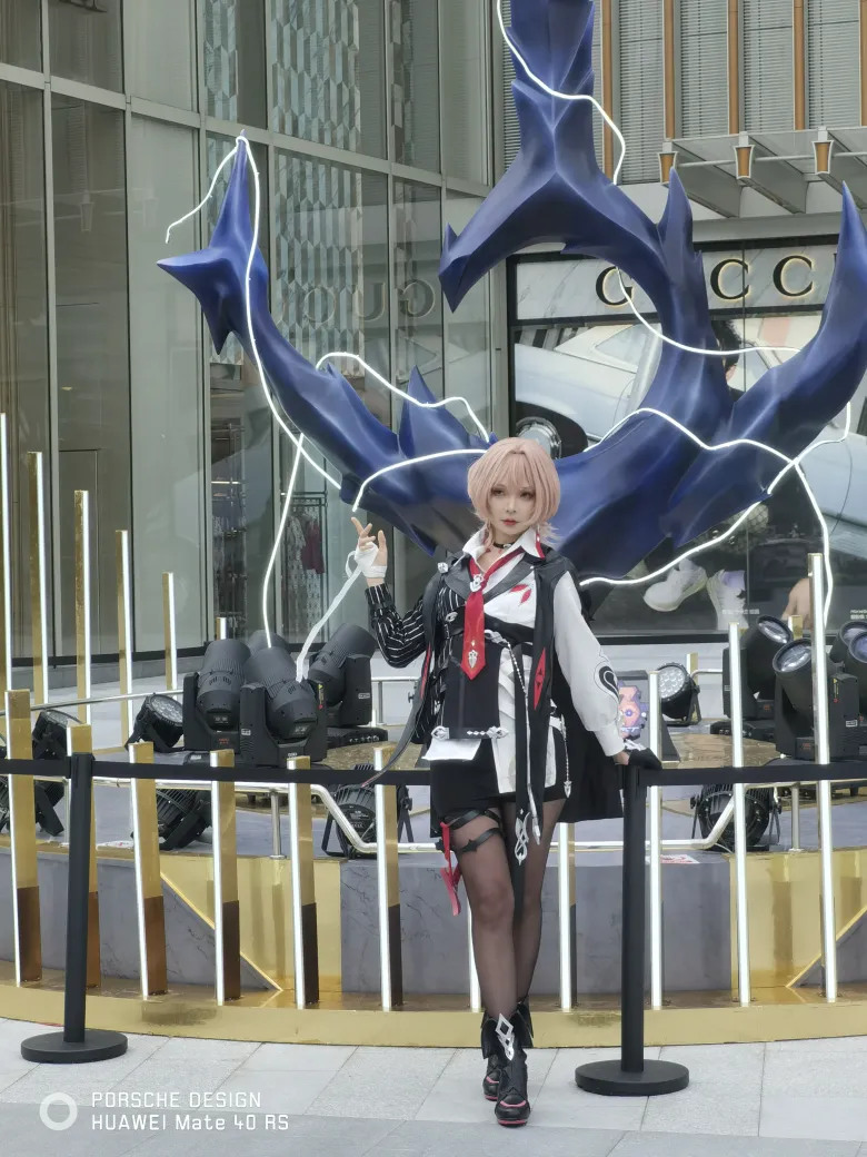 照片：粉色短发的 coser 站在蓝色船锚雕塑前摆姿势，身穿黑白配色的制服。