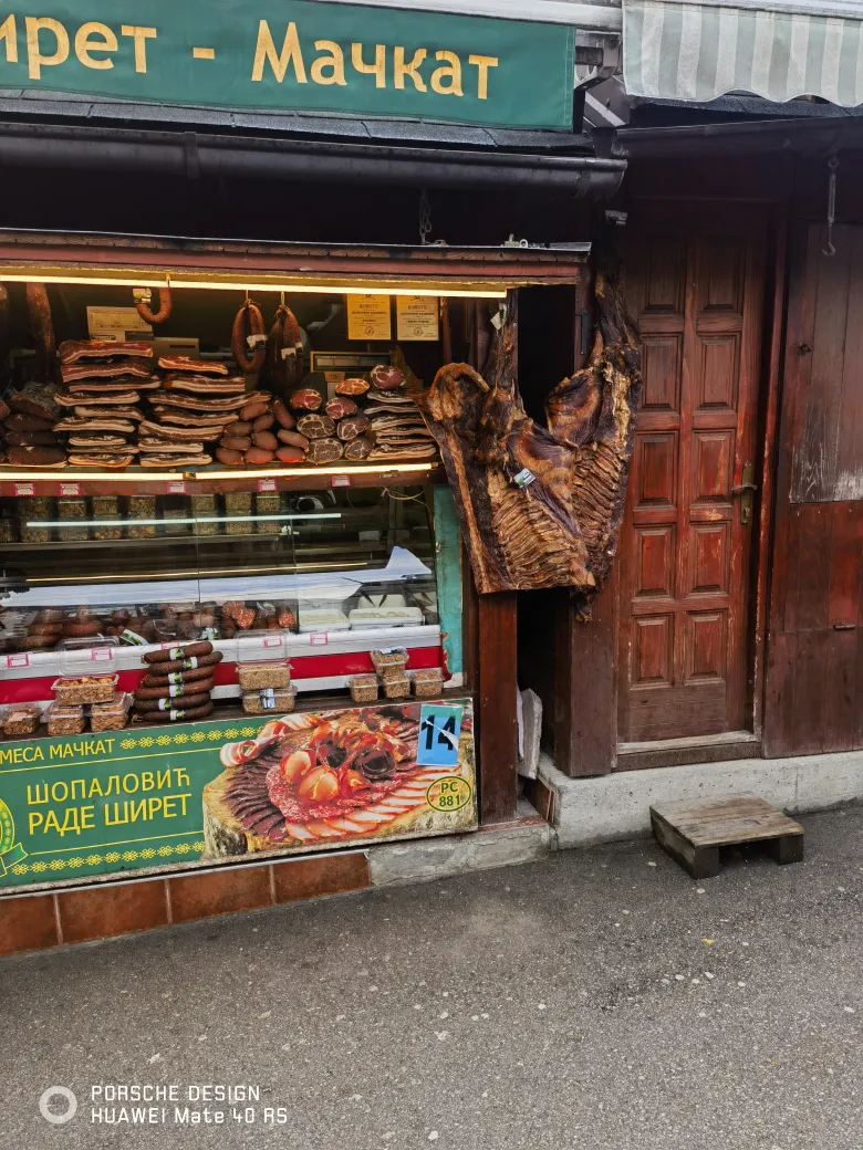 照片：路边肉店的橱窗挂满腌肉、香肠与整块火腿，招牌是塞尔维亚文。
