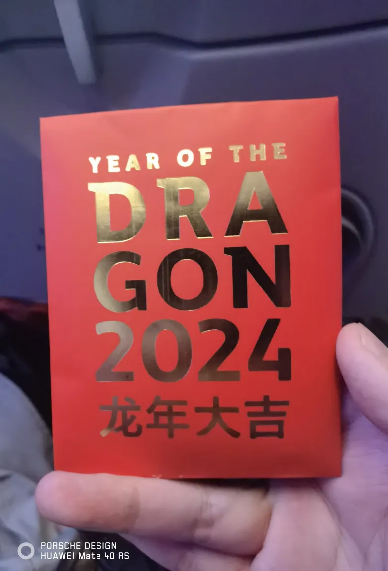 照片：手中拿着卡塔尔航空的红色龙年红包，印着金色 YEAR OF THE DRAGON 2024 与「龙年大吉」。