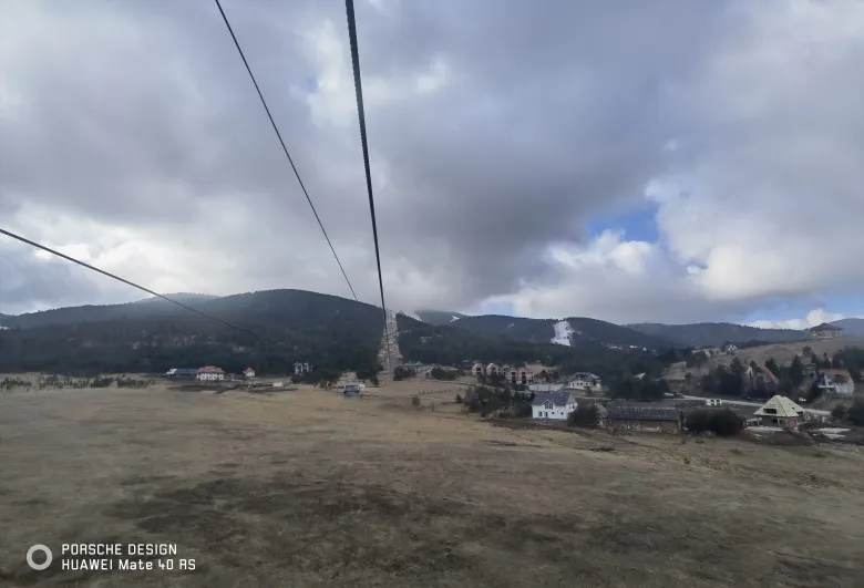 照片：山脚村庄的红顶房屋散落在草坡间，上方是交错的索道缆绳。