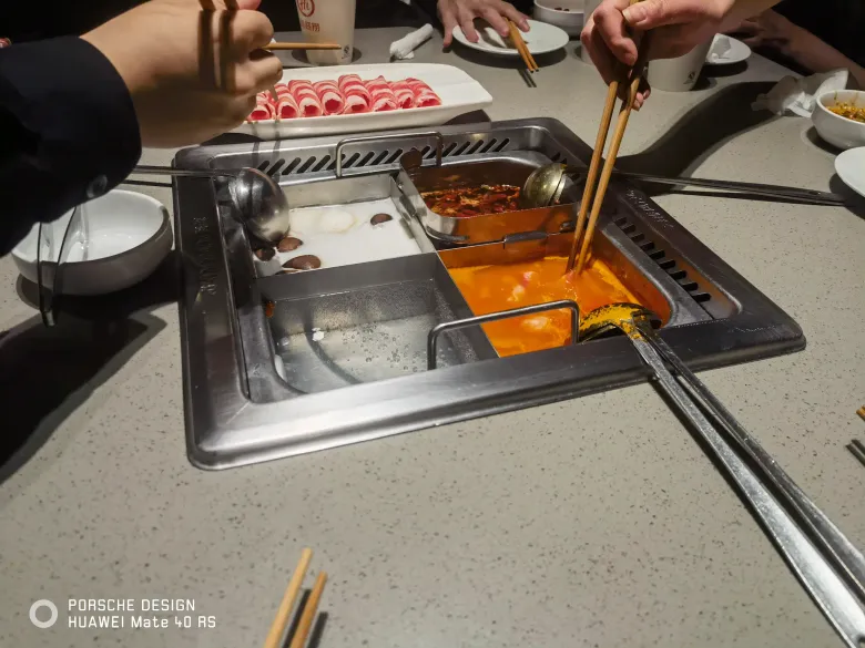 照片：海底捞火锅餐桌，鸳鸯锅冒着热气，手拿筷子夹起食材，旁边是肥牛卷。