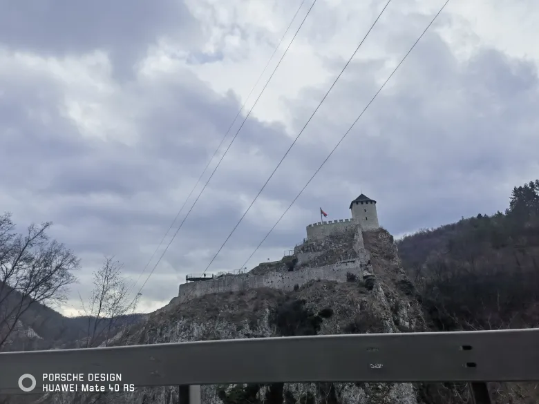 照片：灰色天空下，一座白色钟楼矗立在岩石山丘上，城墙沿山脊延伸。