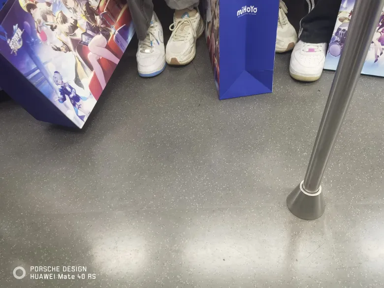 照片：地铁车厢地板上放着印有 miHoYo 标志与角色图案的纸质手提袋。