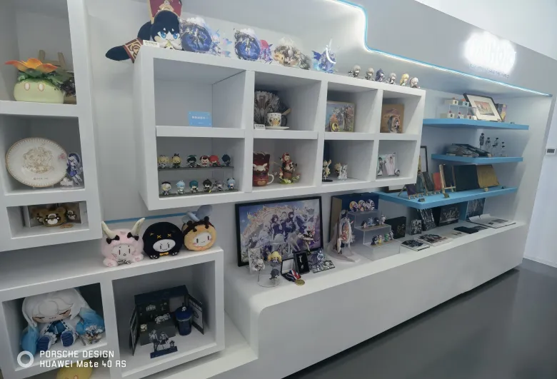 照片：米哈游周边展示墙，格架里摆满角色手办、徽章与玩偶，还有立牌与画册。