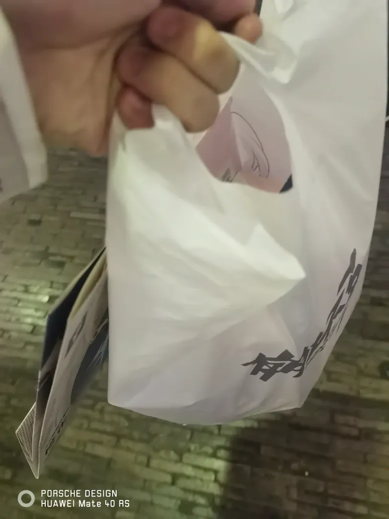 照片：手中拎着印有黑色字样与角色图案的白色周边购物袋。