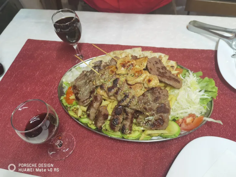 照片：老城餐馆的晚餐，大盘烤肉配土豆、黄瓜与卷心菜沙拉，旁边是两杯红酒。