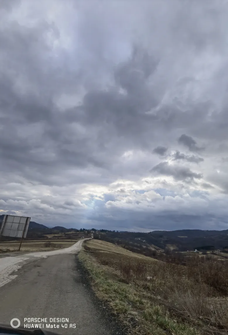照片：车窗外乡间小路通向远处山丘，厚重的云层低沉压顶。