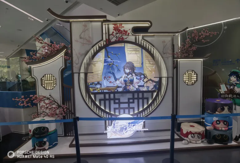 照片：商场里的《崩坏：星穹铁道》展台，圆形画框中是阮梅立绘，旁边堆着猫猫糕玩偶。