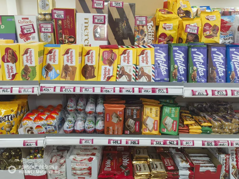 照片：超市货架上摆满 Milka 巧克力、Raffaello 等糖果，标价以第纳尔计。